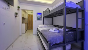 A bunk bed room with a kitchen area, a door, and a wall-mounted clock. - 8A - Alexandros Apartment by SDR (Paralia)
