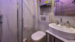 A bathroom with a glass shower enclosure, a toilet, a sink with a mirror, and a towel rack. - 8A - Alexandros Apartment by SDR (Paralia)