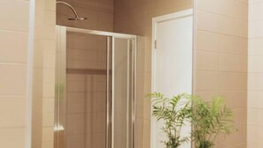 Een badkamer met een grote spiegel, douche, wastafel en een kamerplant.
