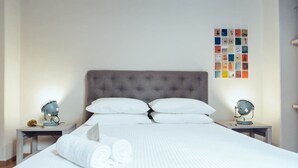 A neatly made bed with white linens, a tufted headboard, and two bedside lamps on nightstands. - we saw athens from 1b (Αθήνα)