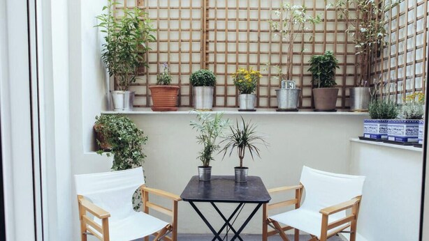A small patio with a table and chairs, surrounded by potted plants on shelves. - we saw athens from 1b (Αθήνα)