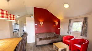 Un espace de vie compact comprenant un coin cuisine, un canapé, une table à manger et un fauteuil rouge.