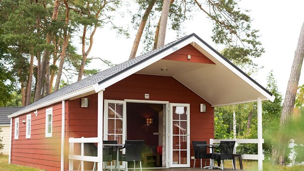 Un bâtiment rouge avec un porche abrité, deux chaises et une petite table.