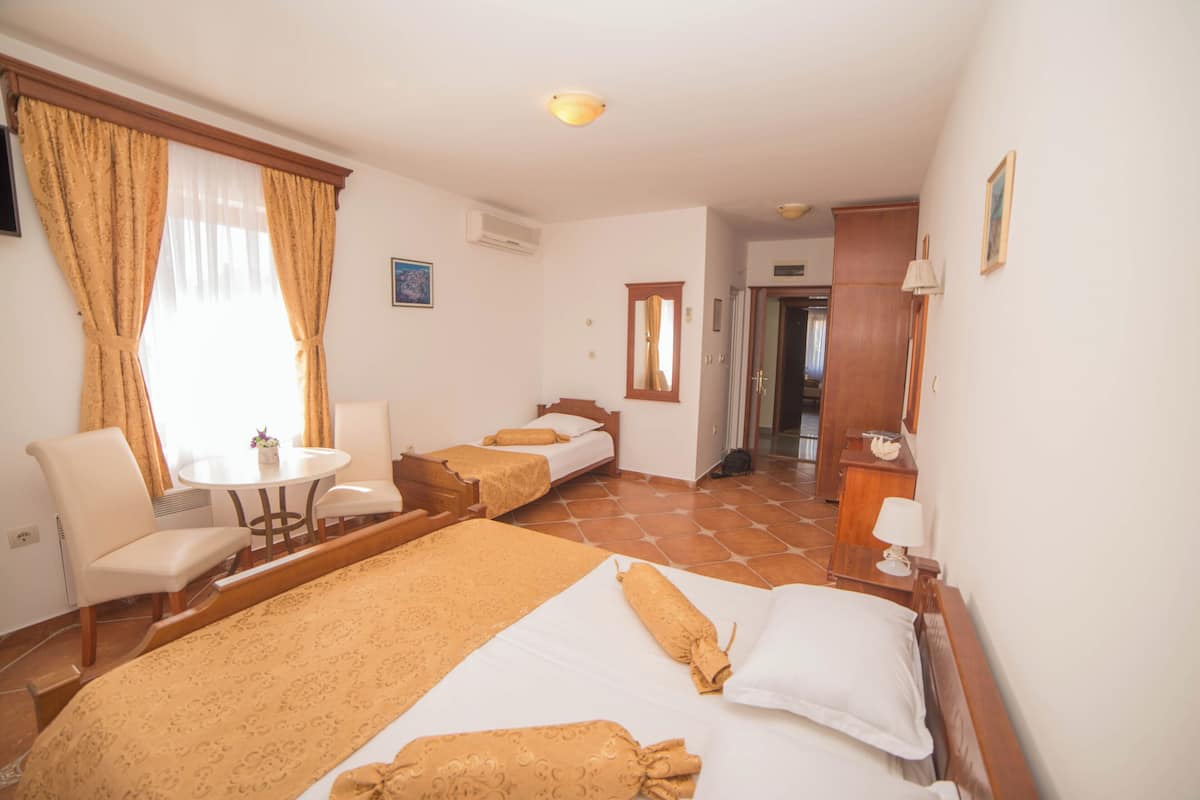 Ein Hotelzimmer mit zwei Betten, einem kleinen Tisch, einem Sessel und einem Schreibtisch mit einer Lampe.