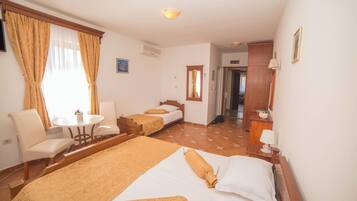 A hotel room with two beds, a small table, a chair, and a desk with a lamp.
