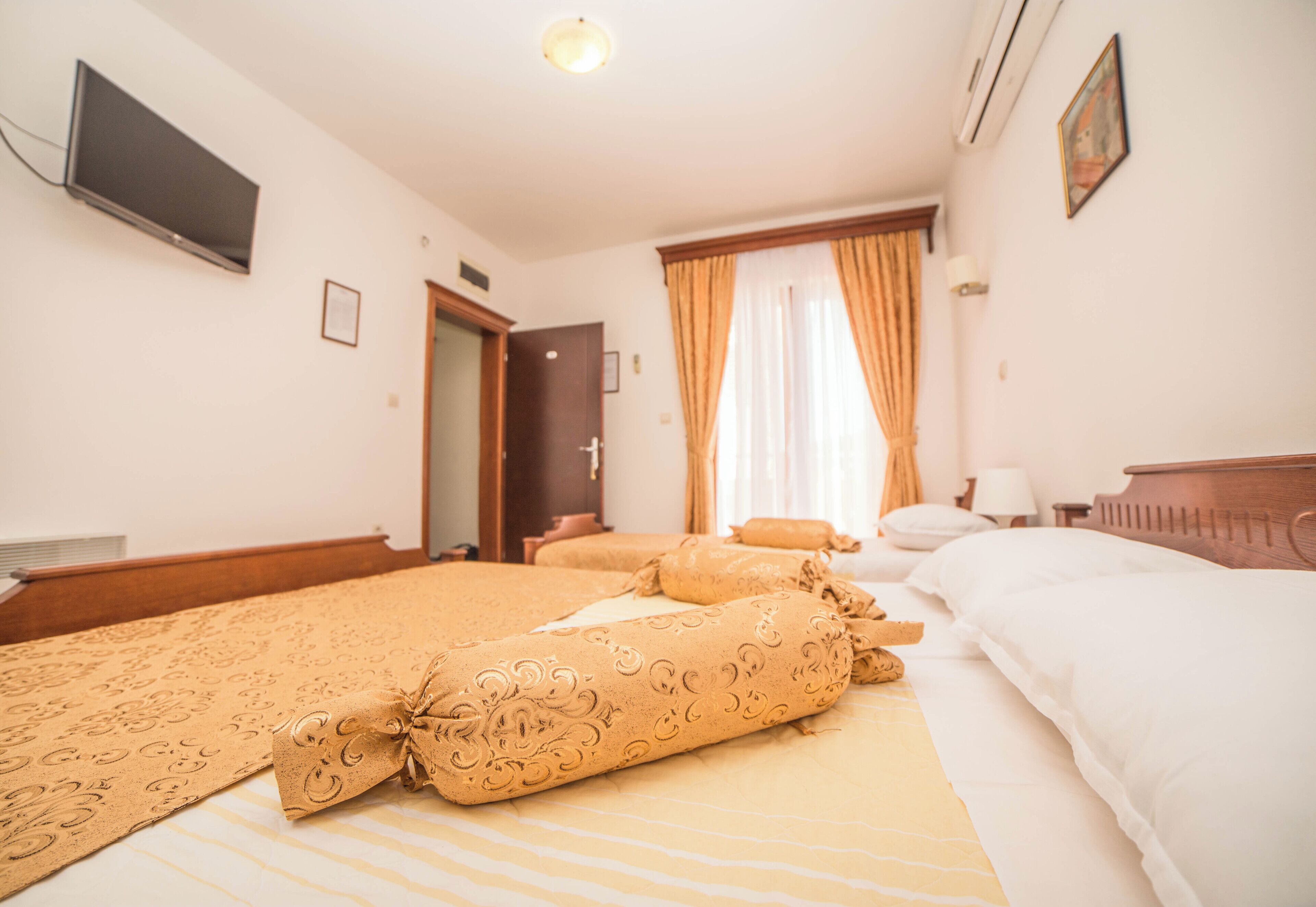 Ein Hotelzimmer mit Bett, Fernseher, Tür und einem fenster mit Vorhängen.