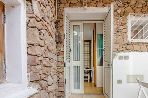 A stone wall, an open door leading to a room with a table and chairs, and a white wall with a window. - GuestHost - A comfortable and welcoming 45 square meters apartment, perfect for two people, located on the lower ground floor of a building without an elevator.The property is ideally located, just a 4-minute walk from the beach: our guests can enjoy the (Golfo Aranci)