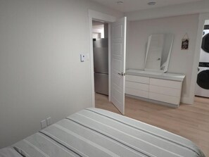 Une chambre à coucher comprenant un lit, une armoire, un miroir et une porte donnant sur la cuisine.