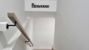 Una escalera con un cartel de 'Bienvenue', escalones de madera y paredes blancas.