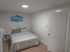 Une chambre à coucher avec un lit, une table de chevet, une œuvre d’art accrochée au mur et une porte blanche.