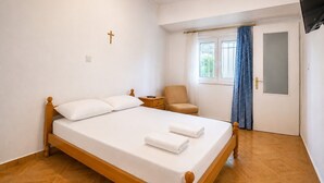 Un dormitorio con cama de madera, una silla, una mesita de noche, un ventanal con cortinas y una puerta.