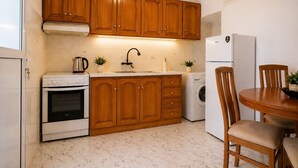 Una cocina compacta con armarios de madera, estufa, lavabo, lavadora y una mesa de comedor con sillas.
