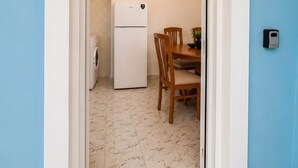 Un pasillo que conduce a una cocina con lavadora, refrigerador y un comedor con sillas y mesa.