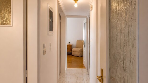 Un pasillo con piso de mármol, una puerta con picaporte dorado y un cuadro en la pared.