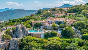 En villa med swimmingpool, omgivet af frodig vegetation og stenede omgivelser.