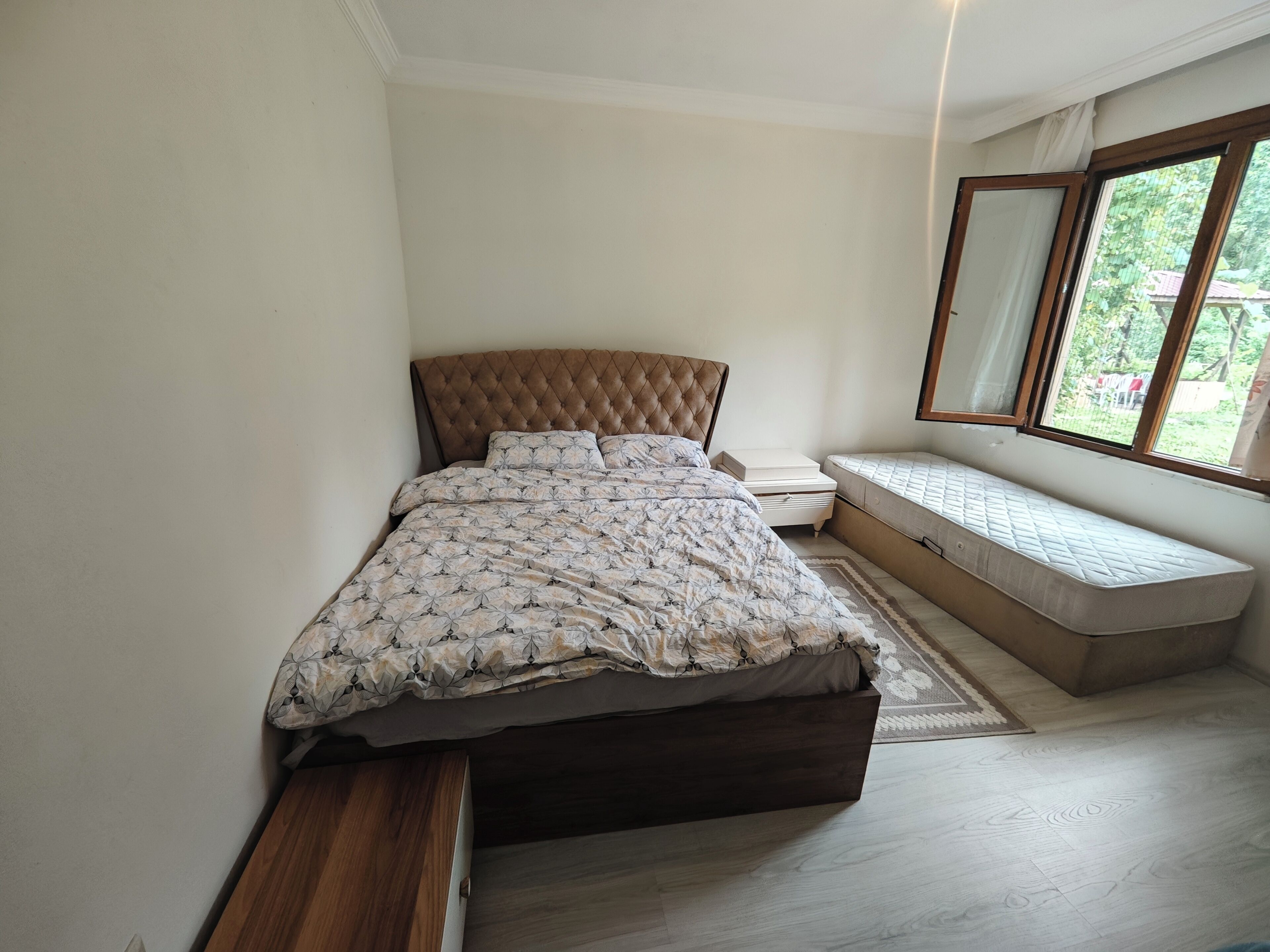 A bedroom with a bed, bedside tables, a bench, and a window with a view.