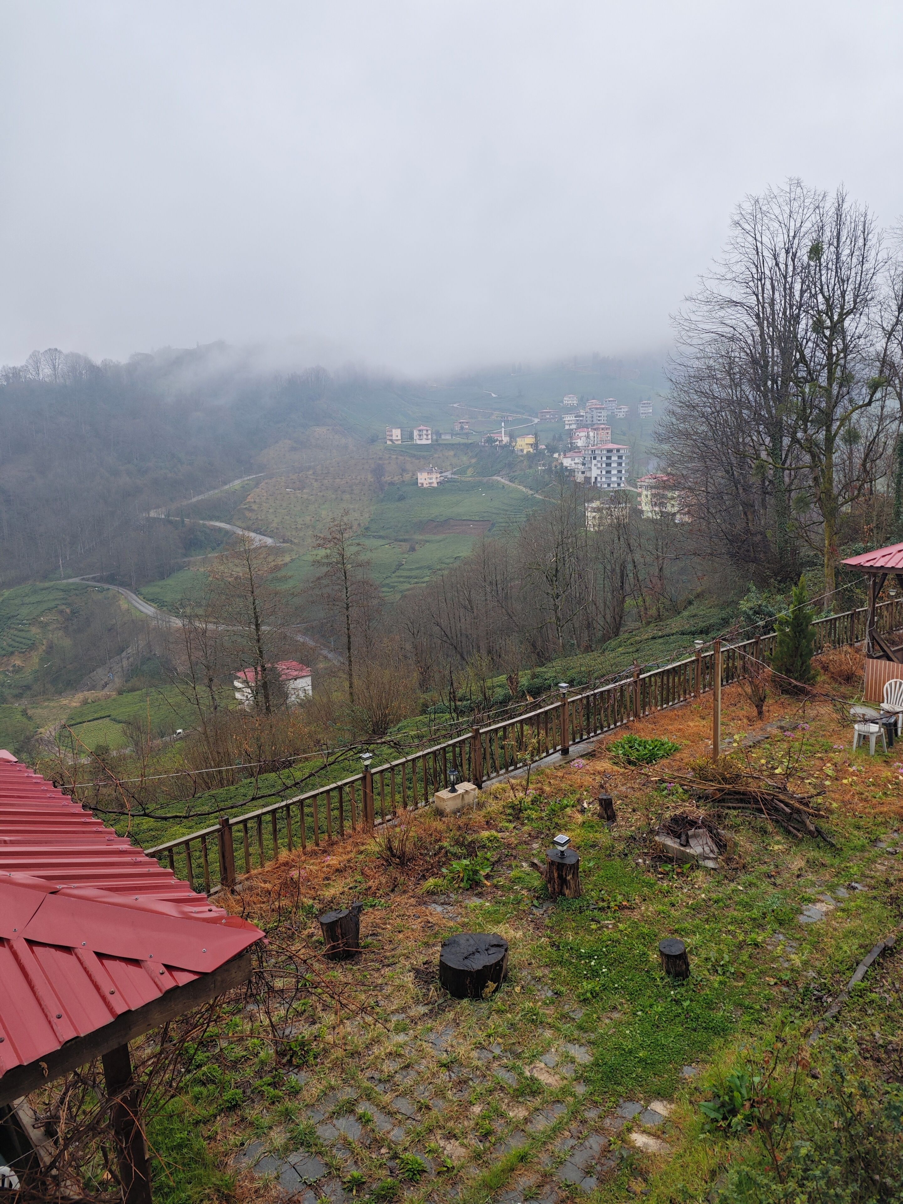 A rural landscape with a winding road, a wooden fence, and a red-roofed structure.