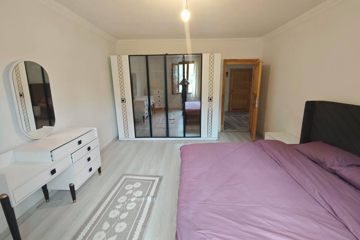 Une chambre à coucher comprenant un lit, une commode, un miroir, une armoire et un couloir menant à une autre pièce.