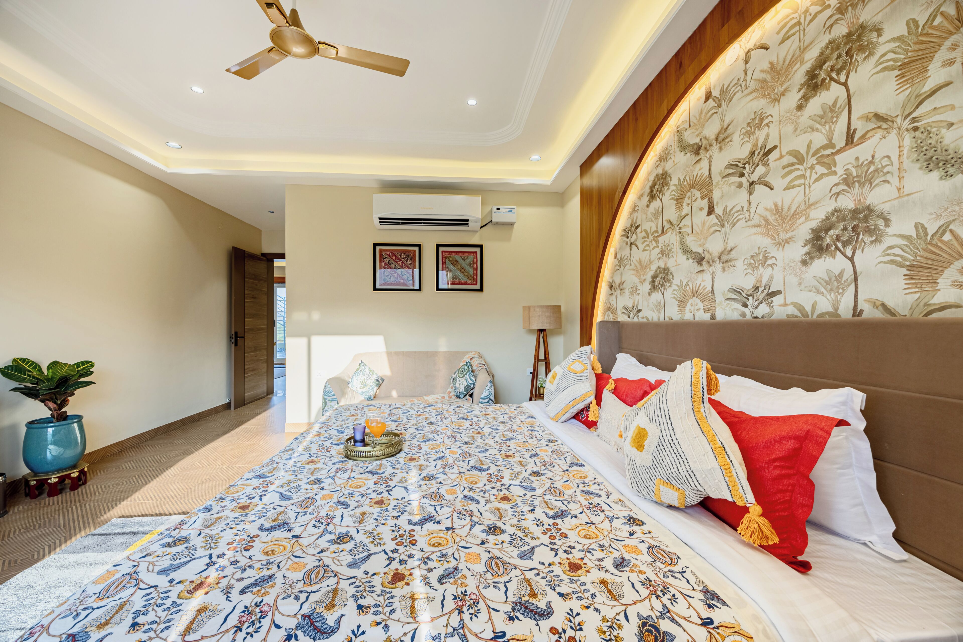 A bedroom with a large bed, a ceiling fan, a wall-mounted air conditioner, and a potted plant.