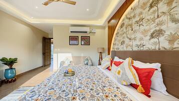A bedroom with a large bed, a ceiling fan, a wall-mounted air conditioner, and a potted plant.