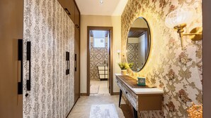 Un pasillo con papel tapiz estampado, un espejo con lámpara y una puerta que da a otra habitación.