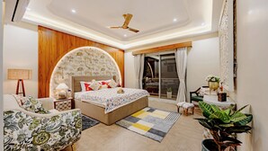 Un dormitorio con cama, sofá, ventilador de techo, ventana con cortinas y una planta en maceta.
