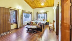 Quarto com teto de madeira, cama com várias almofadas, uma mesinha e uma cadeira.