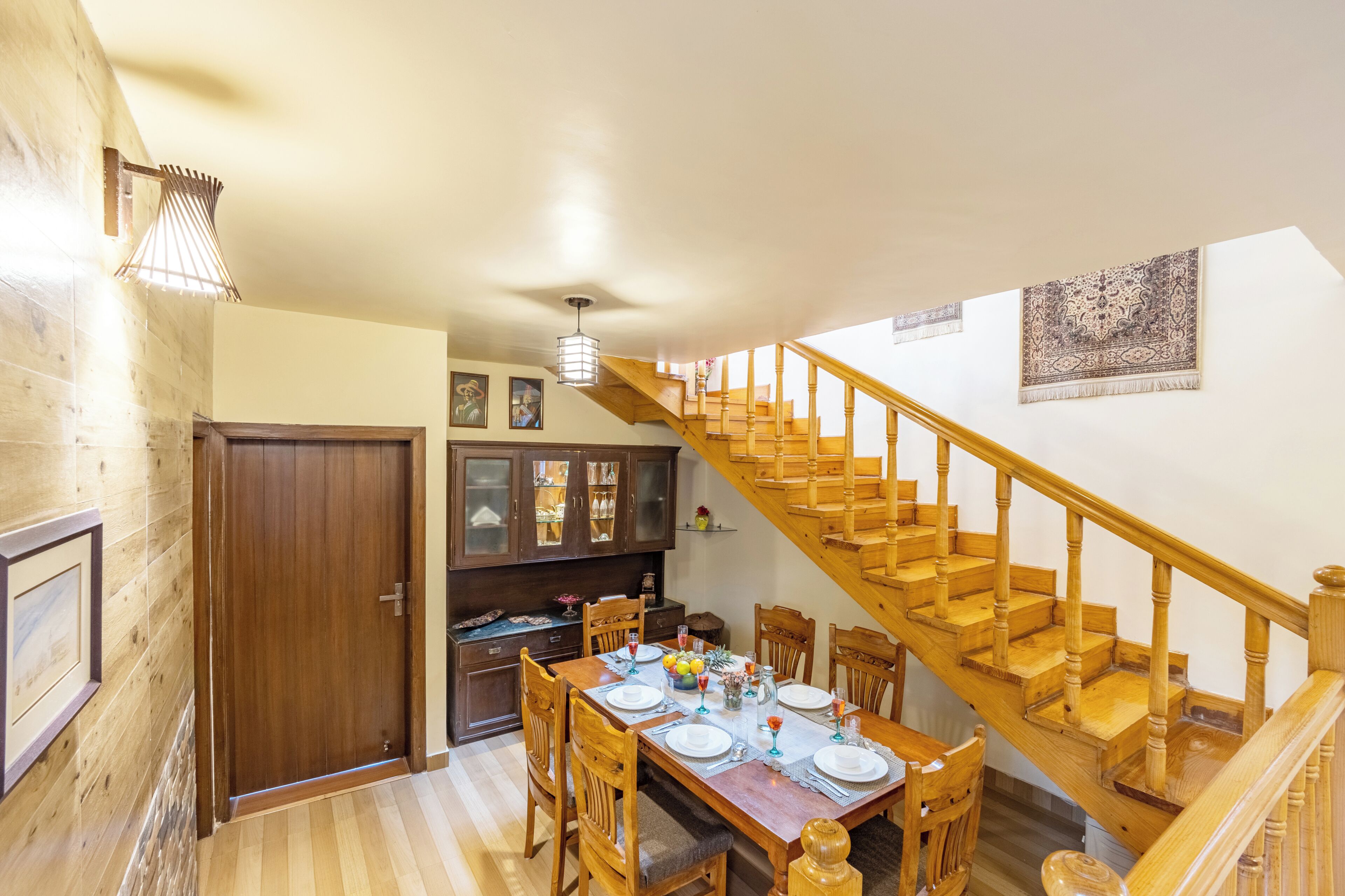 Un coin repas agrémenté d’un escalier en bois, d’une table à manger dressée pour six personnes et d’un buffet en bois aux portes vitrées.