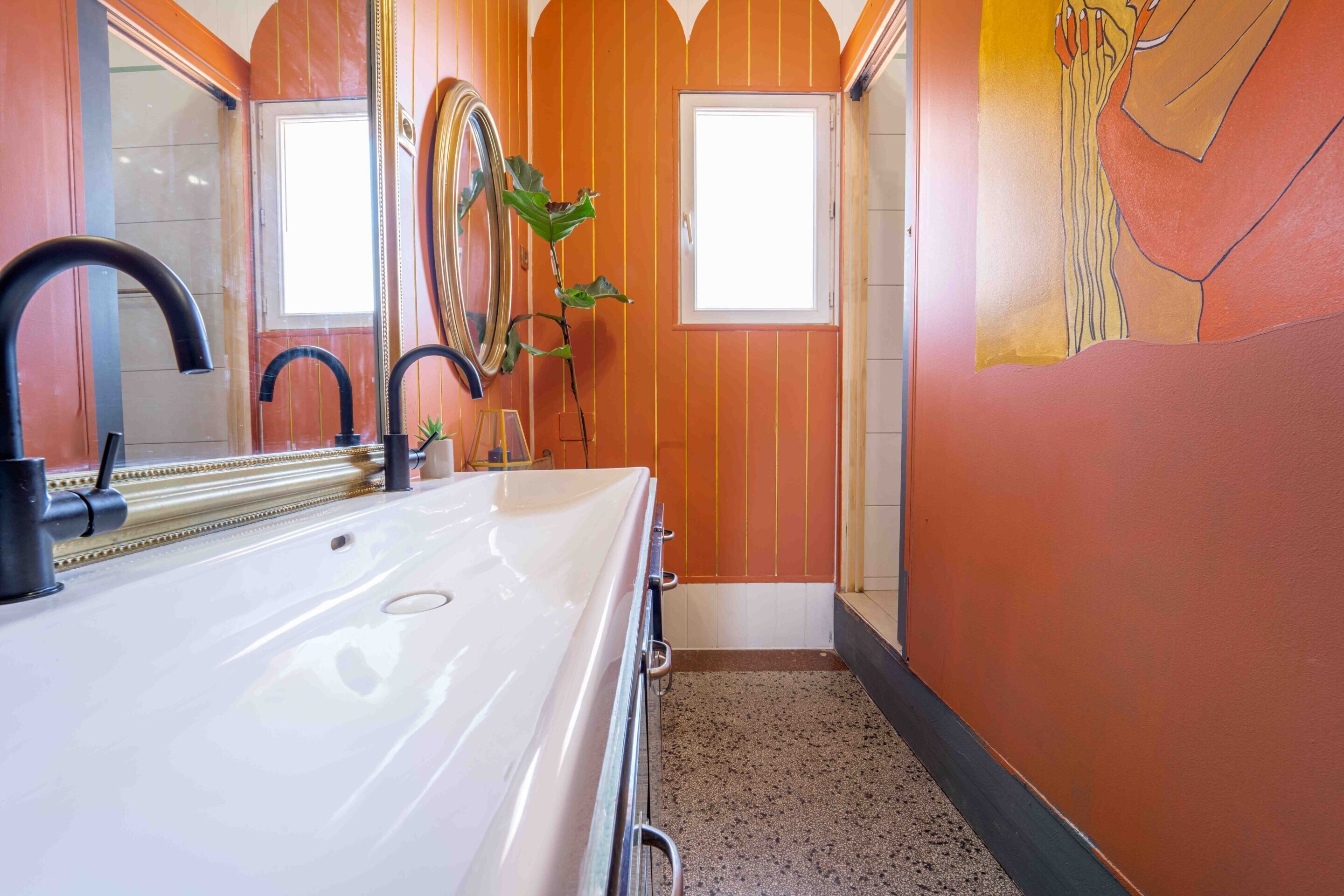 A bathroom with a white sink, two black faucets, a mirror, and a potted plant.