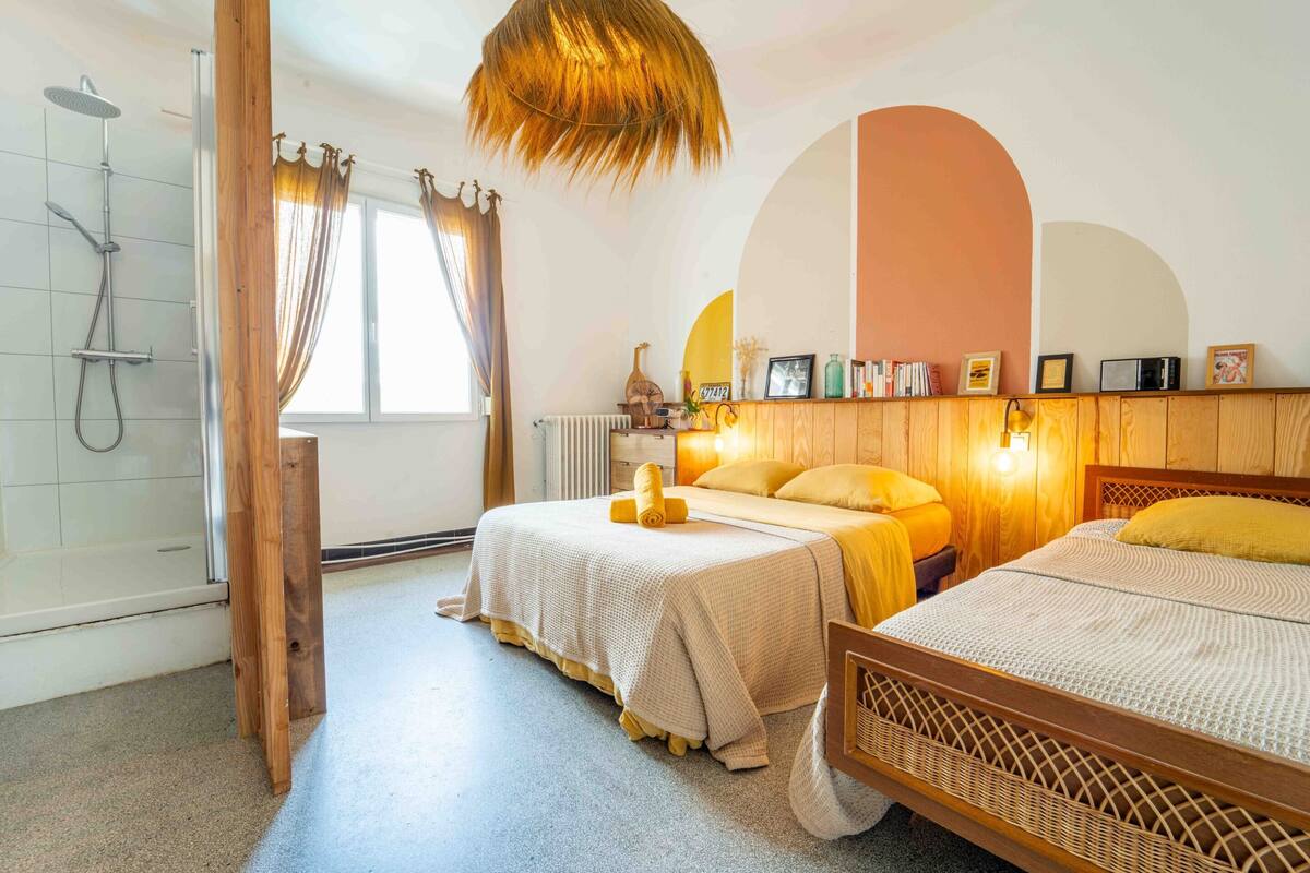 A bedroom with two beds, a wooden headboard, a shower, and a large window with curtains.