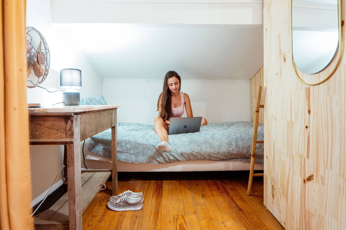 A bedroom with a wooden bed, a desk with a laptop, and a mirror on the wall.