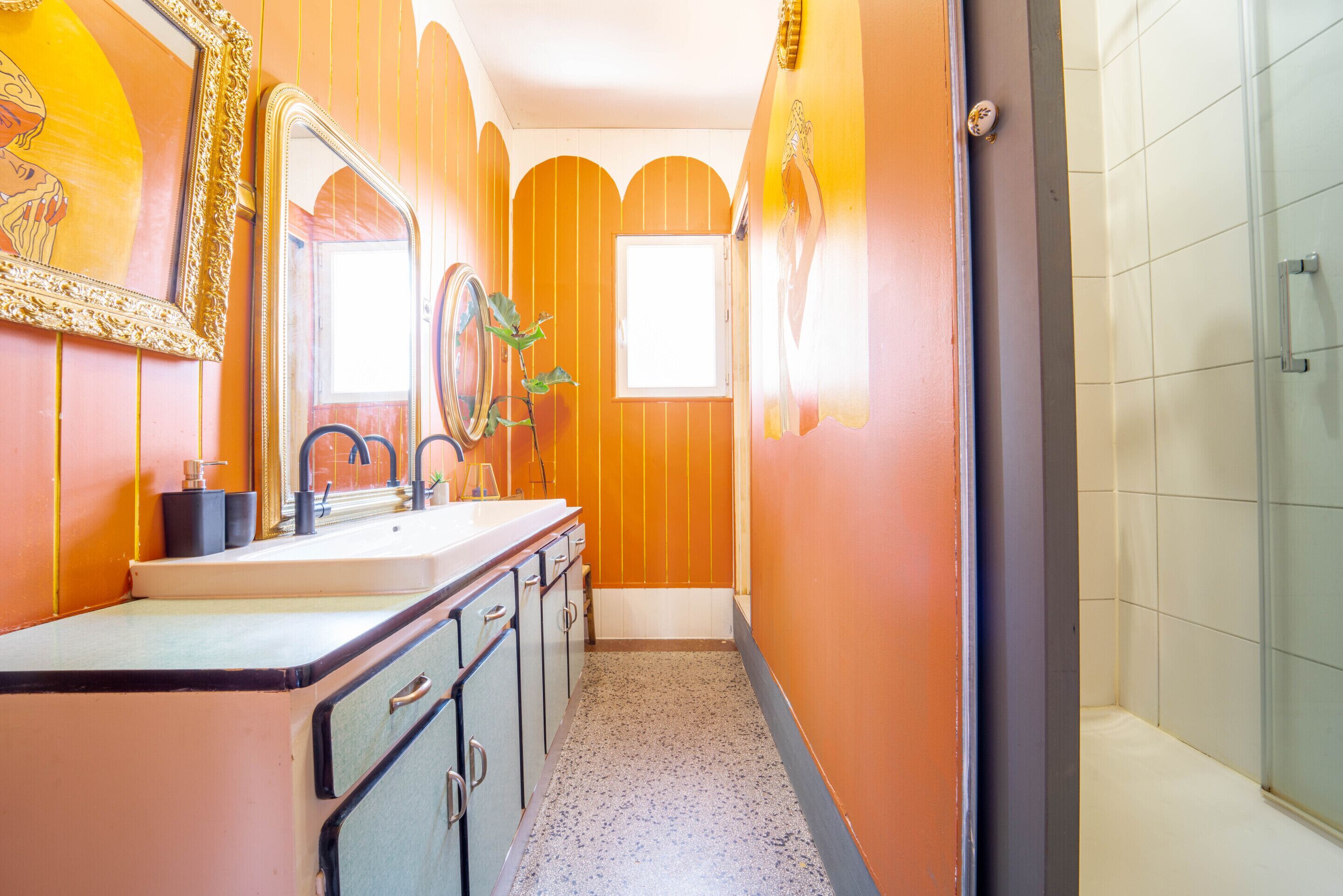 A narrow bathroom with a sink, mirror, and shower.
