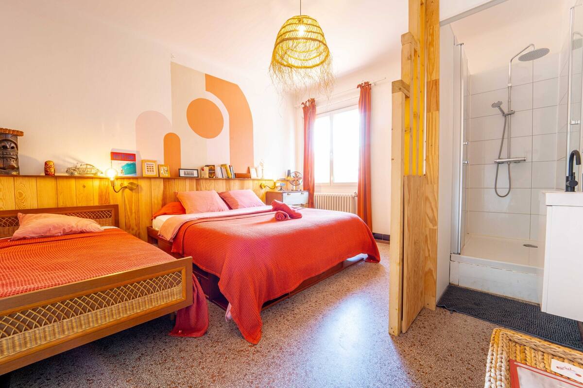 A room with two beds, a shower, and a large window with curtains.
