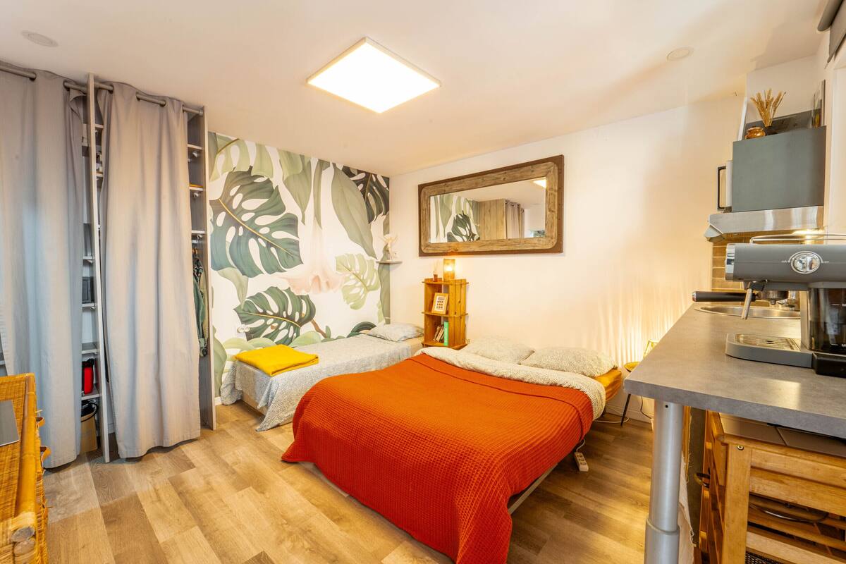 A bedroom with a bed, a desk, a mirror, and a kitchenette.