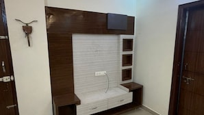 Ein Zimmer mit einer fest eingebauten Holz-Unterhaltungsanlage, einem weiß gefliesten Boden und einer Tür rechts.