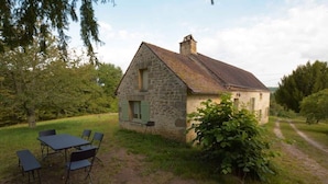 A stone house with a sloped roof, a small porch, and a dining area with a table and chairs. - Les Bardilles*Country house*3km from Sarlat (Sarlat-la-Canéda)