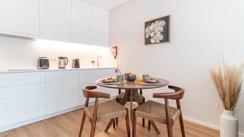 Una cocina moderna con armarios blancos, una mesa redonda con cuatro sillas y un jarrón con plantas secas en el suelo.