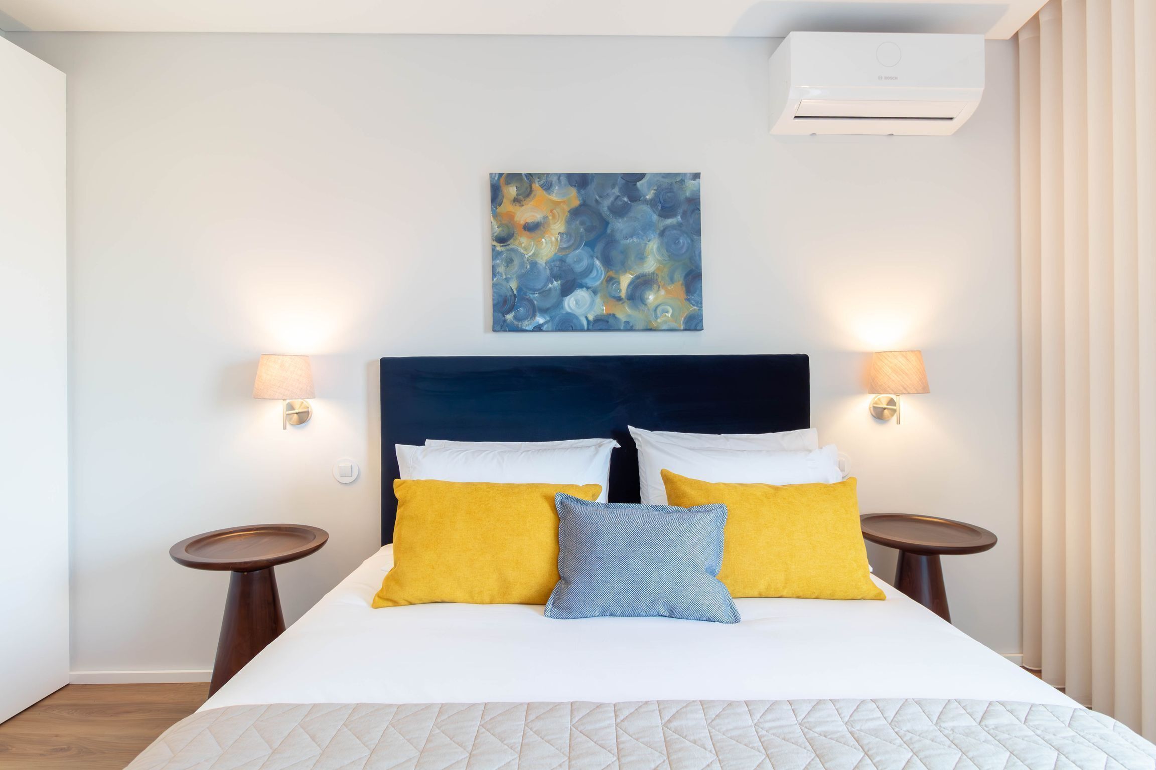 Una habitación de hotel con una cama, dos lámparas de noche, un cuadro en la pared y un equipo de aire acondicionado.