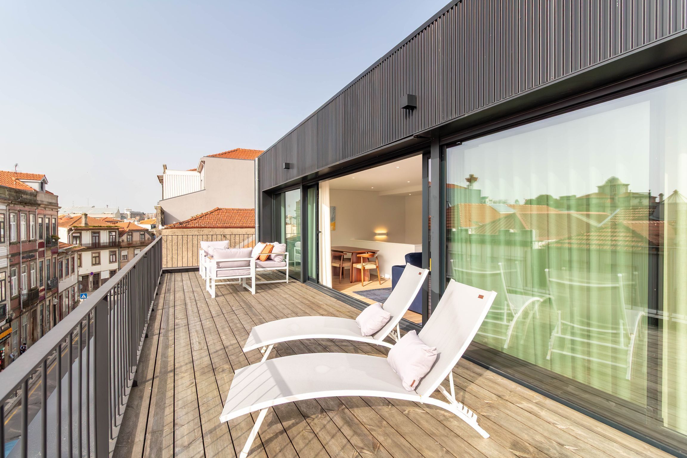 A balcony with two lounge chairs and a table, overlooking a cityscape.