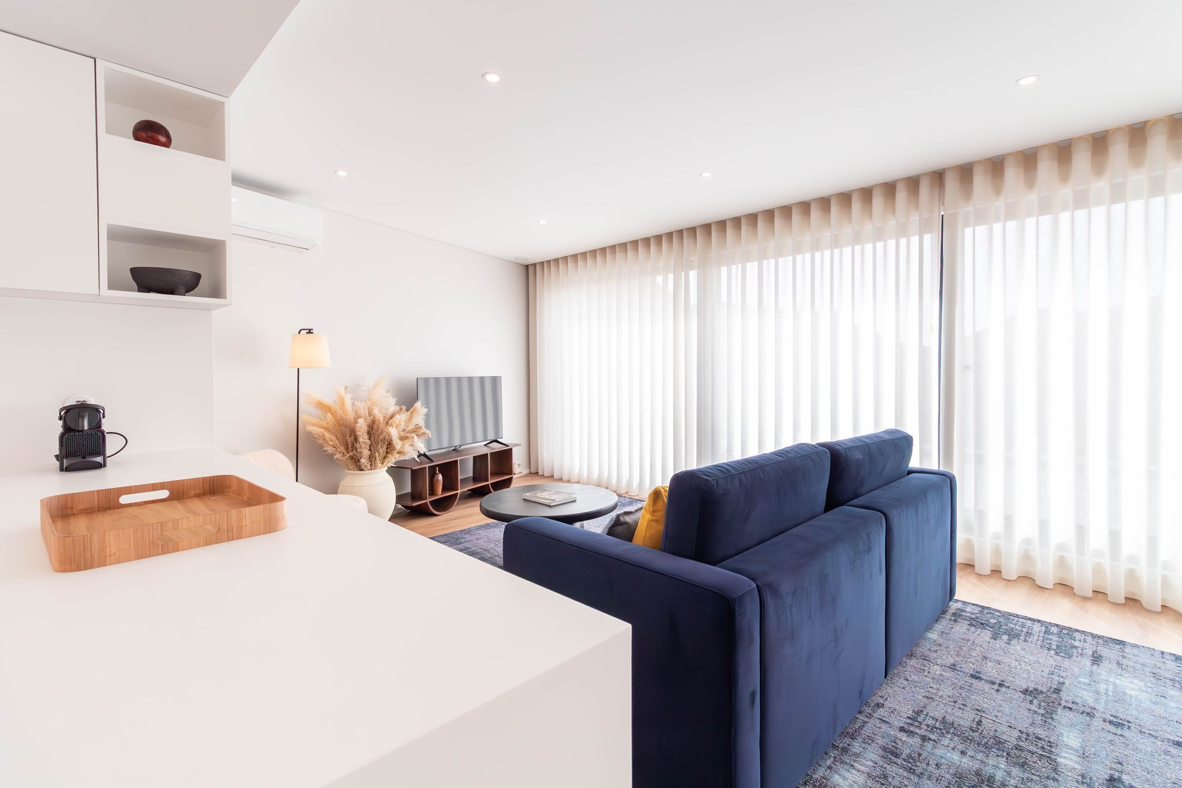 Uma sala de estar moderna com um sofá, uma mesa de centro, uma TV e um espaço de jantar com um aparador de madeira.