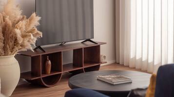 Una sala de estar moderna con un televisor de pantalla plana sobre un soporte de madera, una mesa de centro redonda con una revista y un jarrón con plantas secas.