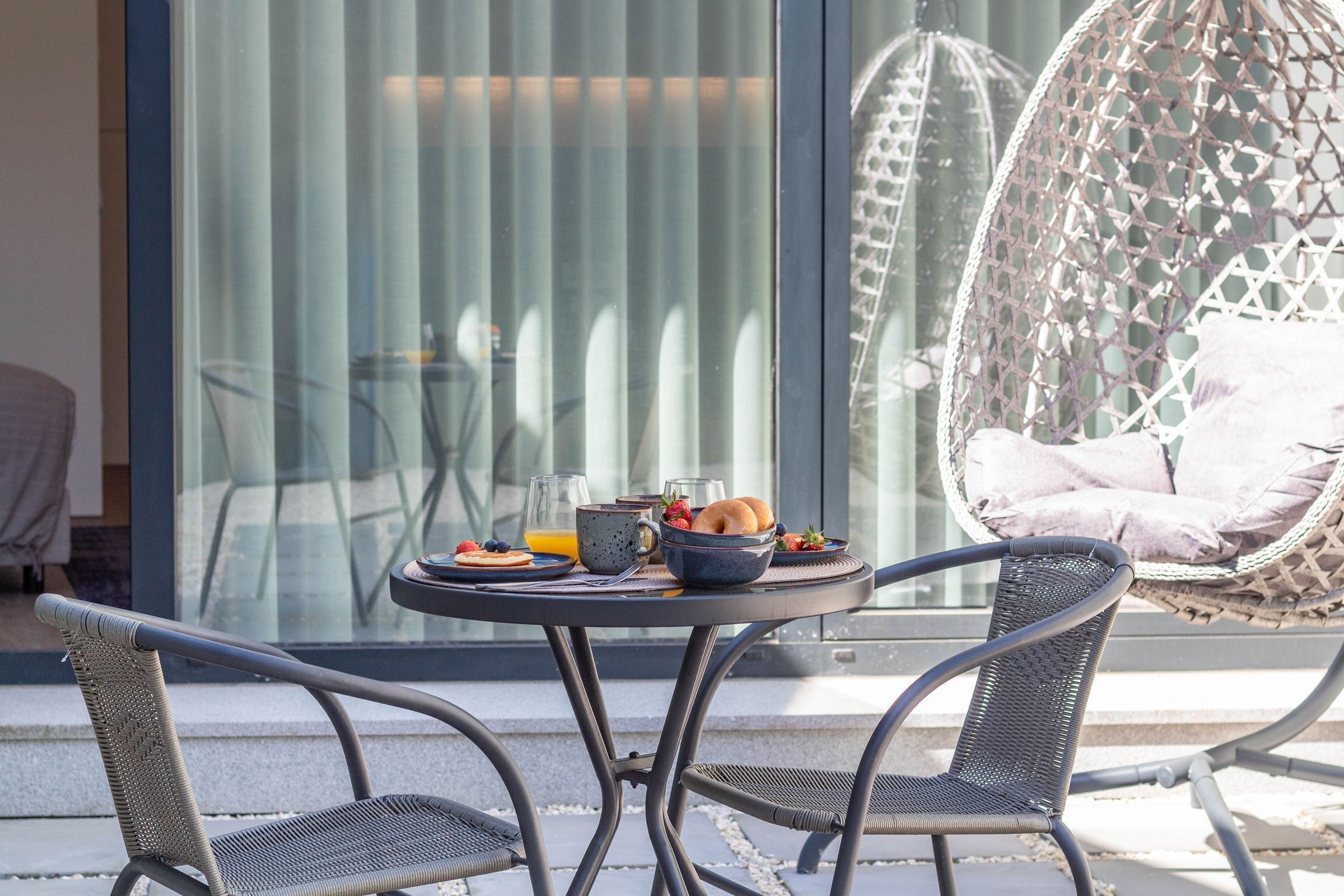 A dining area with a round table, two chairs, and a hanging chair with cushions.