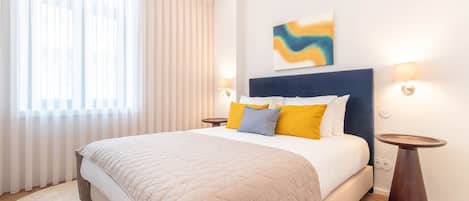 A hotel room with a large bed, a bedside table, a lamp, and a window with curtains.