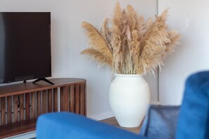 Un televisor sobre un soporte de madera, un jarrón blanco con plumas de pluma de páramo y un sofá azul.