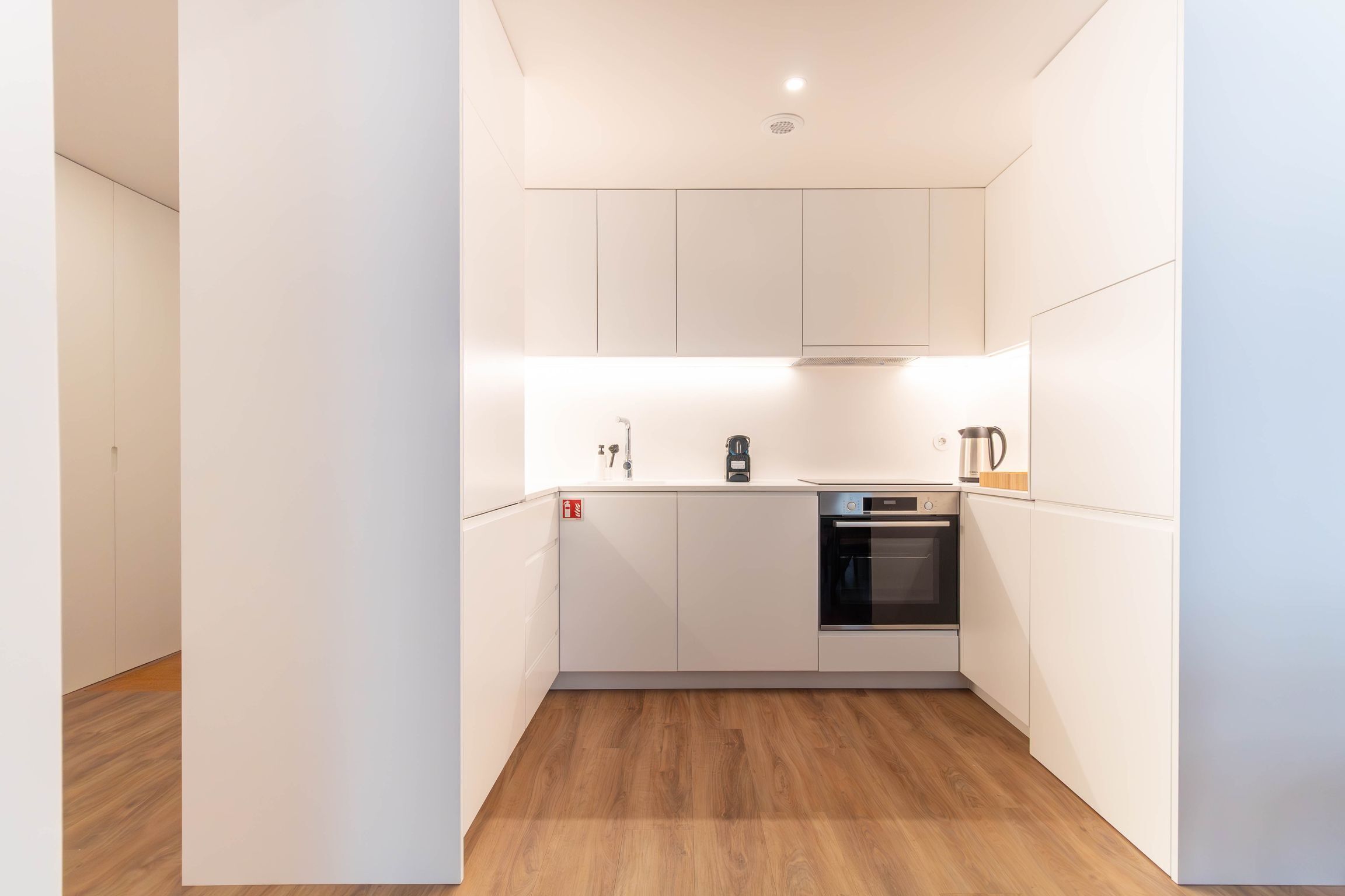 A modern kitchen with white cabinetry, a built-in oven, and a coffee maker.