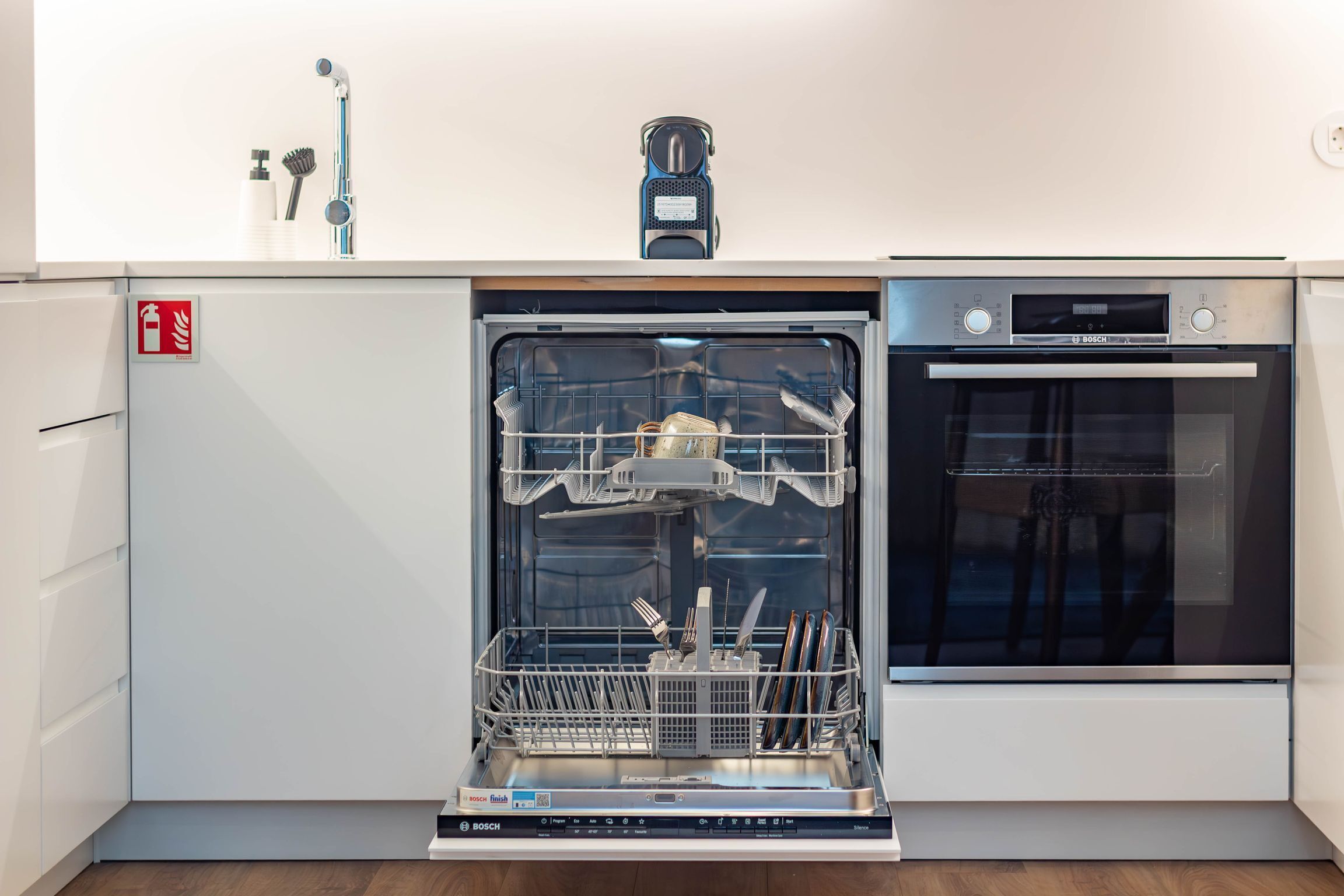 Uma cozinha compacta com máquina de lavar louça, forno e pia com torneira.