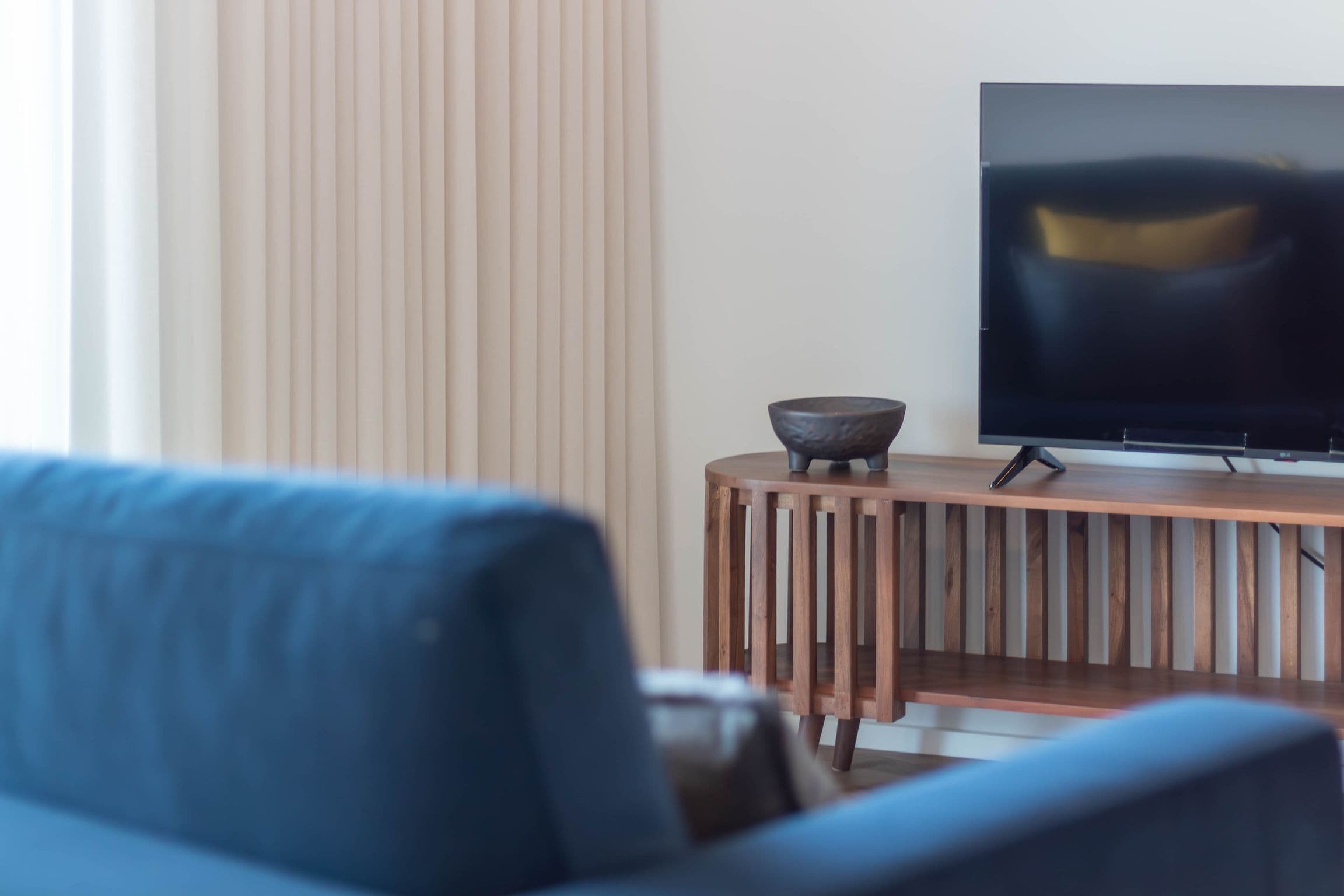 Una sala de estar moderna con un sofá, un televisor sobre un mueble de madera y un cuenco decorativo.