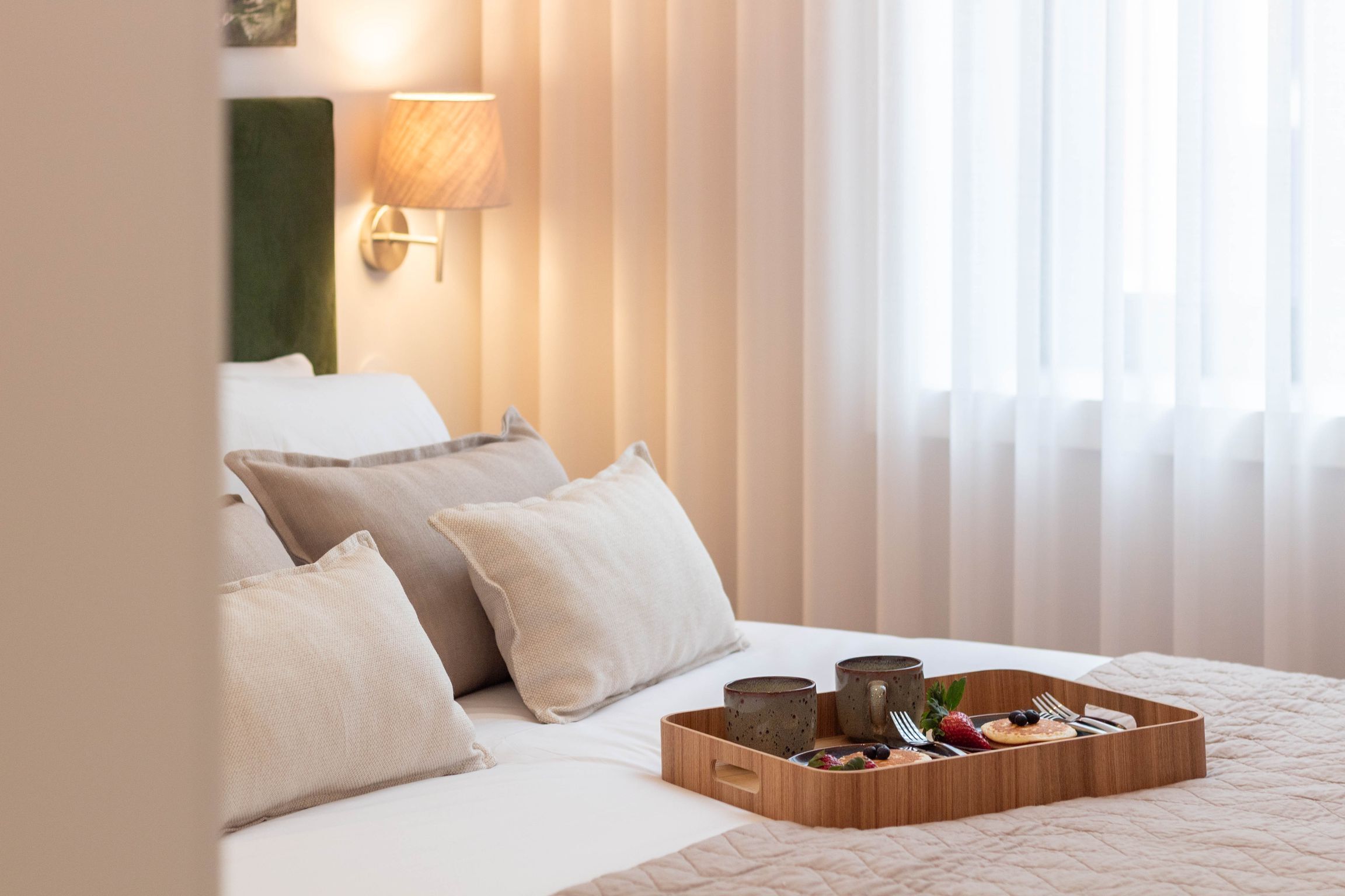 Habitació d'hotel amb llit, almoinades, un safata amb articles per a l'esmorzar i una finestra amb cortines.