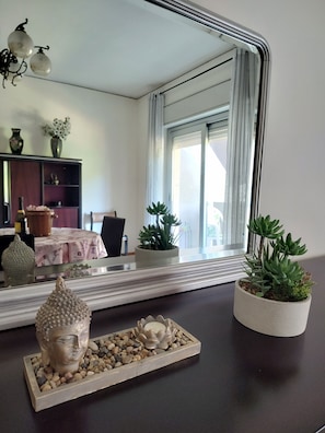 Une pièce dotée d’un grand miroir qui reflète un coin repas, une statue de Bouddha et deux plantes en pot, le tout posé sur une surface sombre.