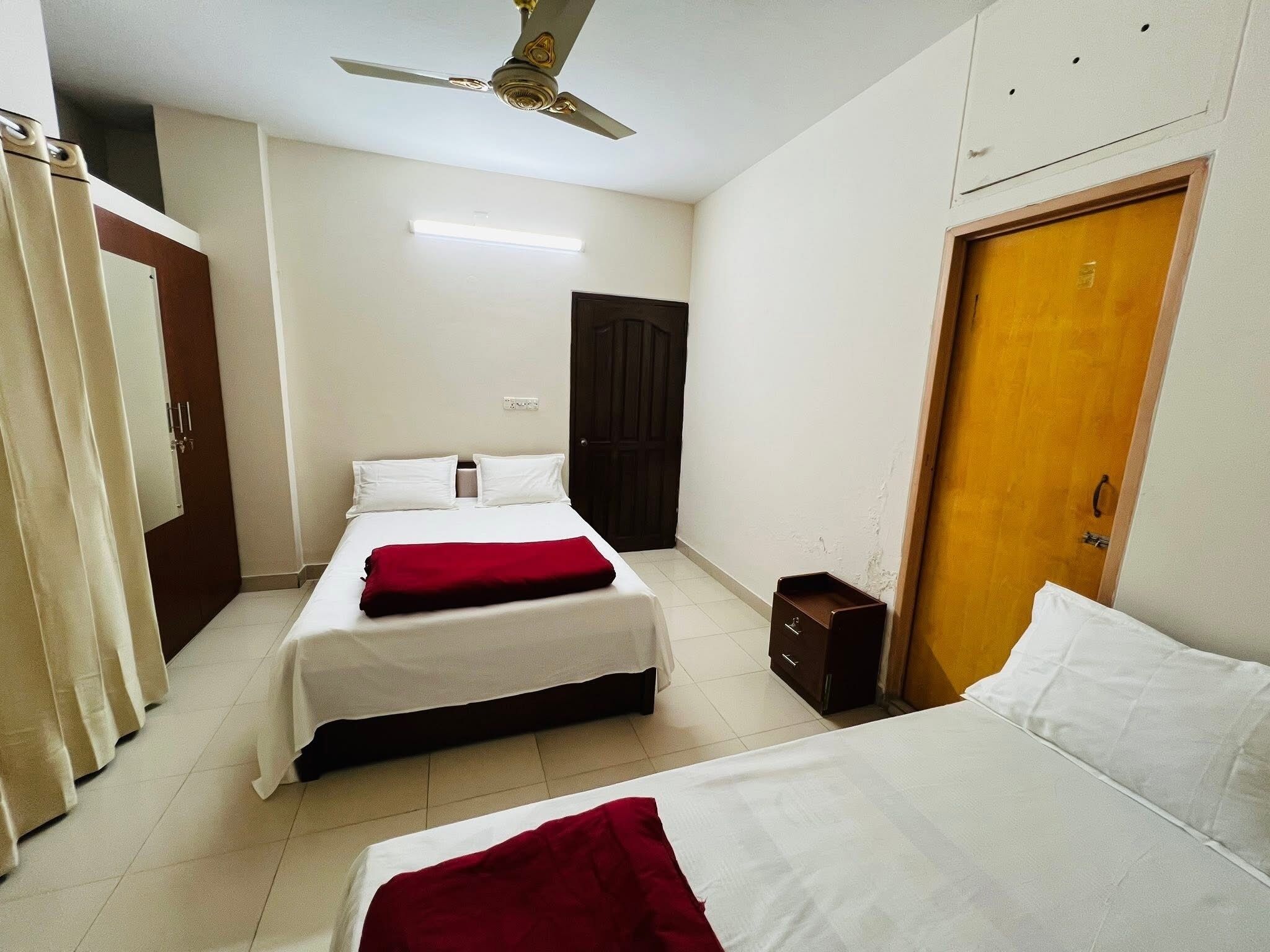A bedroom with two beds, a ceiling fan, a wardrobe, and a door.